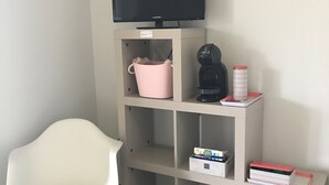 Um quarto com uma cadeira branca, uma televisão em uma prateleira, uma cafeteira e caixas organizadoras.