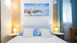 A hotel room with a large bed, two bedside tables with lamps, a painting of a lighthouse, and a view of the sea. - Apartments Nada (Dubrovnik)
