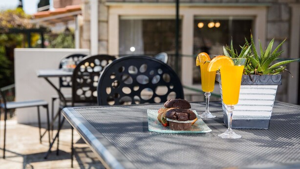 An outdoor dining area with a table set for two, featuring a chocolate cupcake and two glasses of orange juice. - Apartments Nada (Dubrovnik)