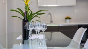 A glass table with a bottle and glasses, a plant, and a kitchen in the background. - Apartments Nada (Dubrovnik)