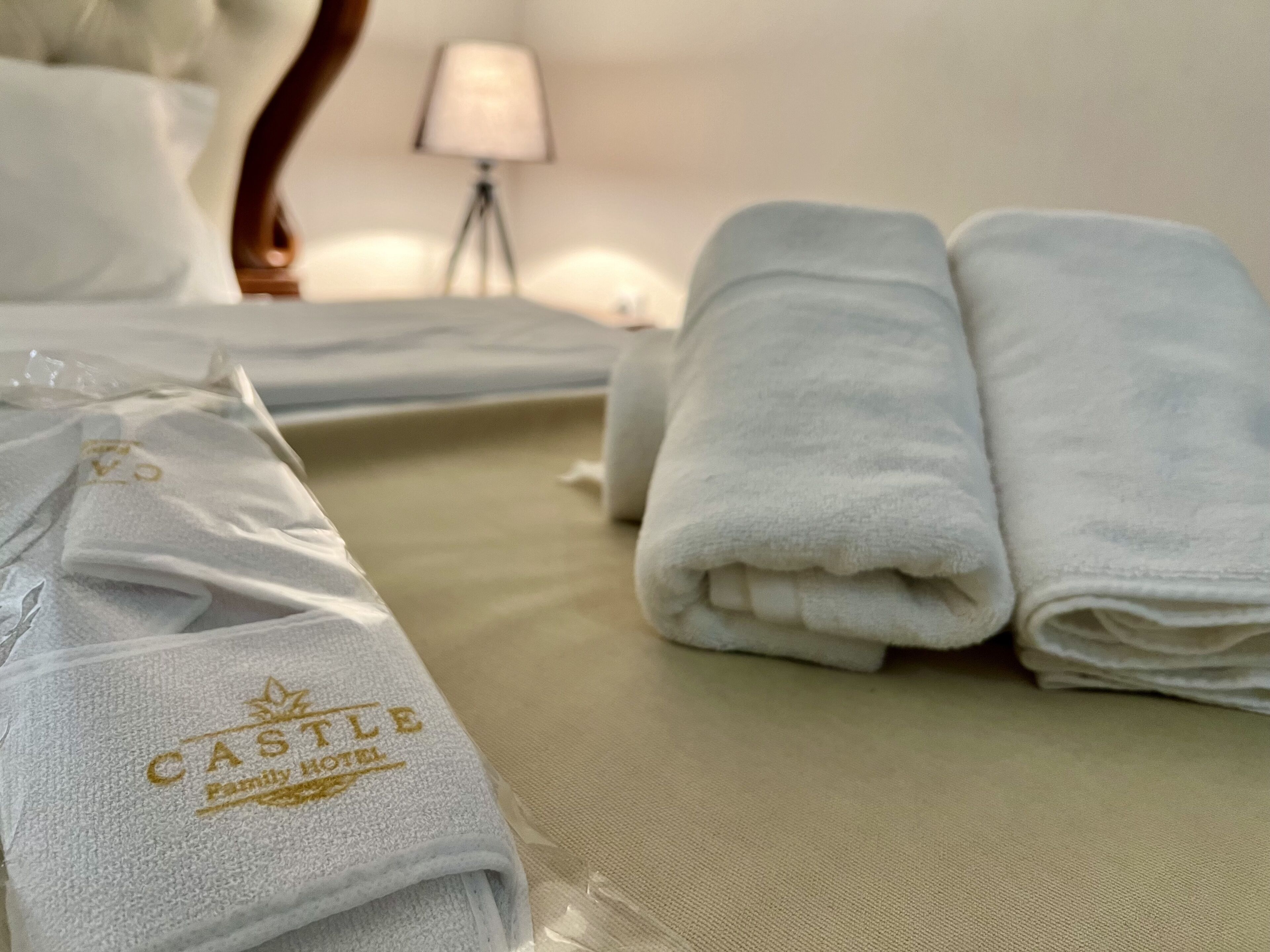 A neatly made bed with white linens and a towel with "CASTLE FAMILY HOTEL" embroidered on it.