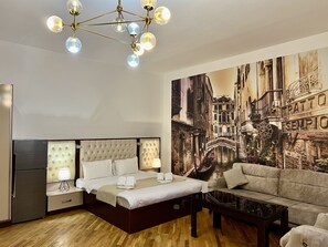 Habitación de hotel con cama, sofá, mesa de centro de vidrio y un mural de un paisaje urbano.