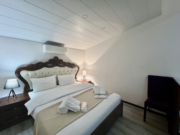 Una cama bien hecha con sábanas blancas, cabecera de madera y lámpara de noche.