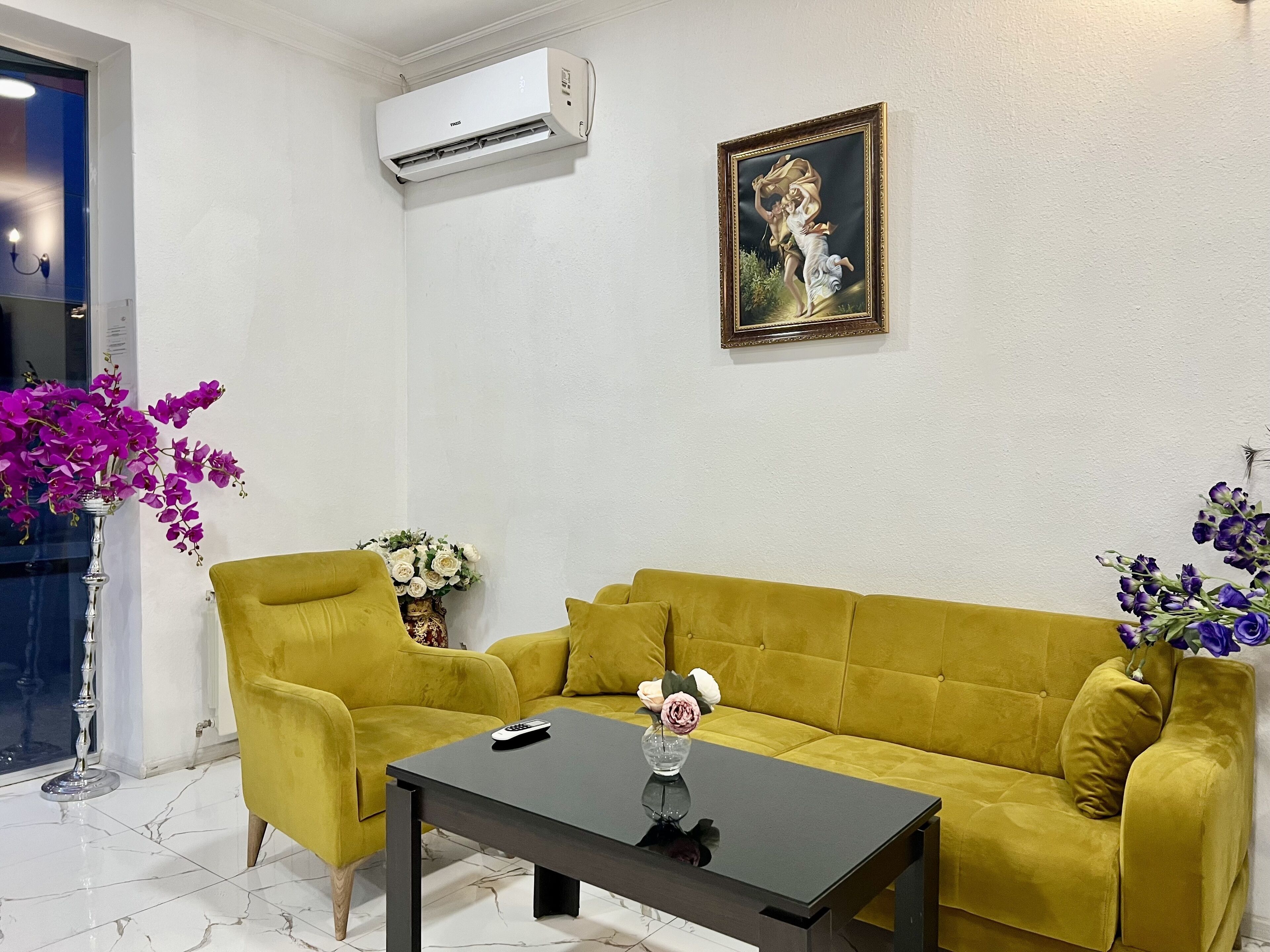 A living room with a yellow sofa, a black coffee table, and a painting on the wall.