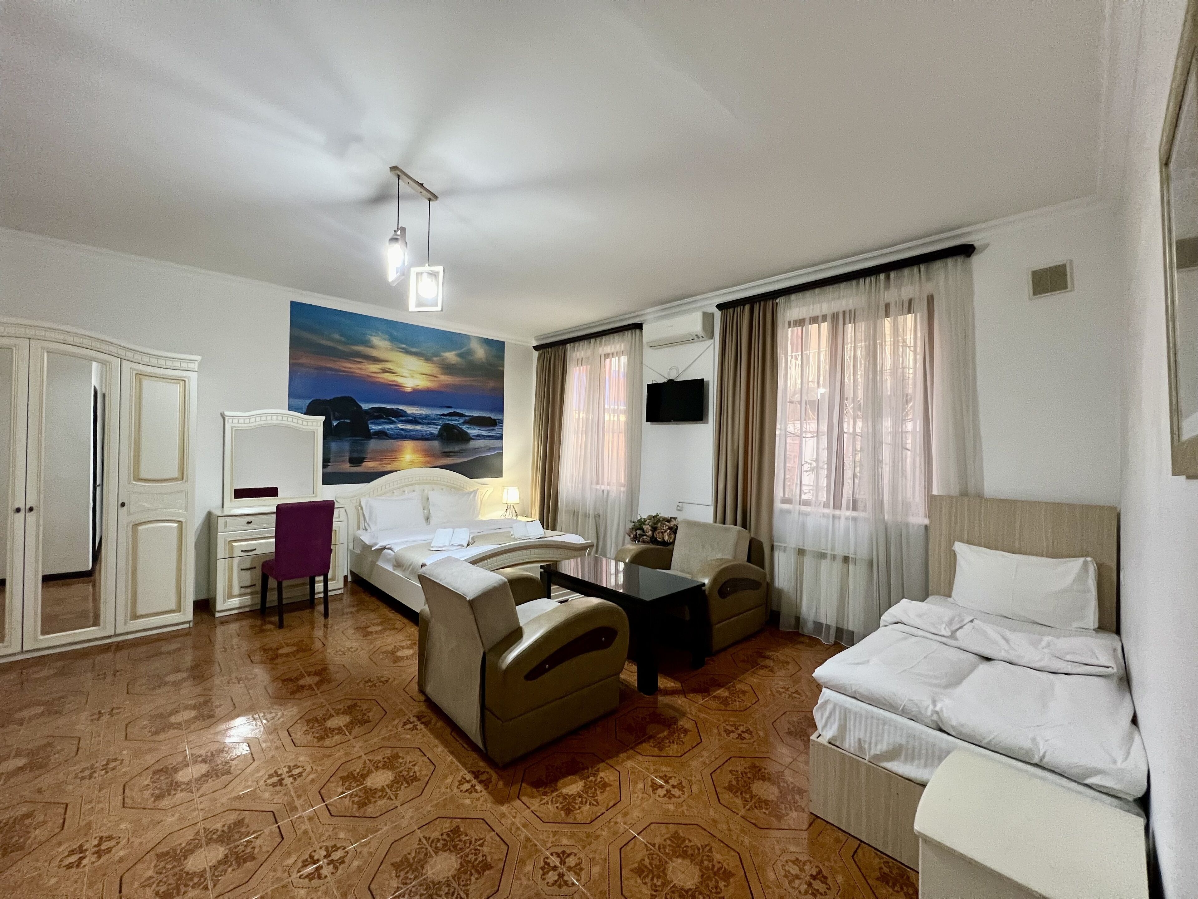 Ein Hotelzimmer mit Bett, Sofa, Schreibtisch und Stuhl. Ein Gemälde hängt an der Wand und ein Fernseher ist dort montiert.
