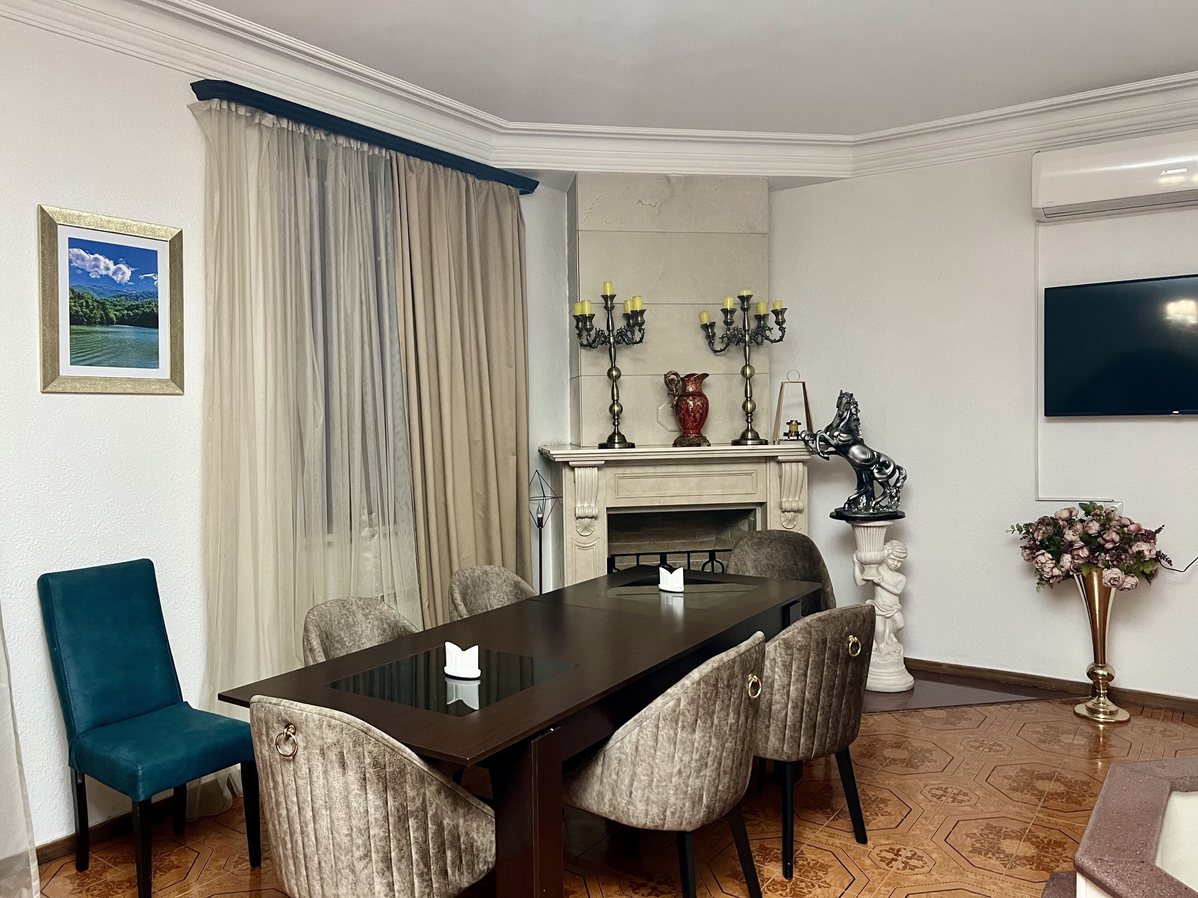 Camera d'albergo con tavolo da pranzo, sedie, camino, televisore e un quadro appeso al muro.