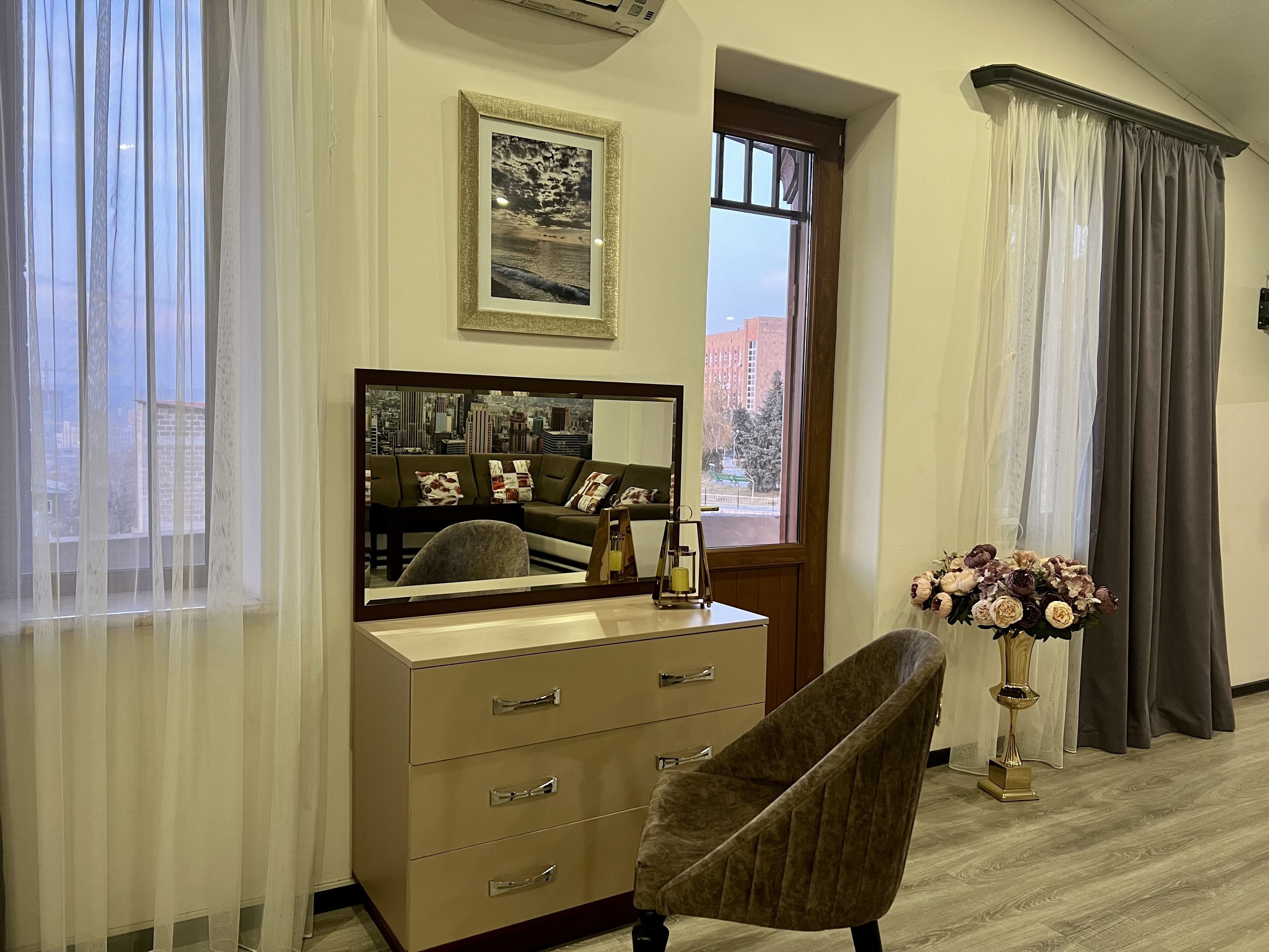 Una habitación con un espejo grande, un aparador, una silla y una ventana con cortinas.