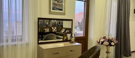 Una habitación con un espejo grande, un aparador, una silla y una ventana con cortinas.