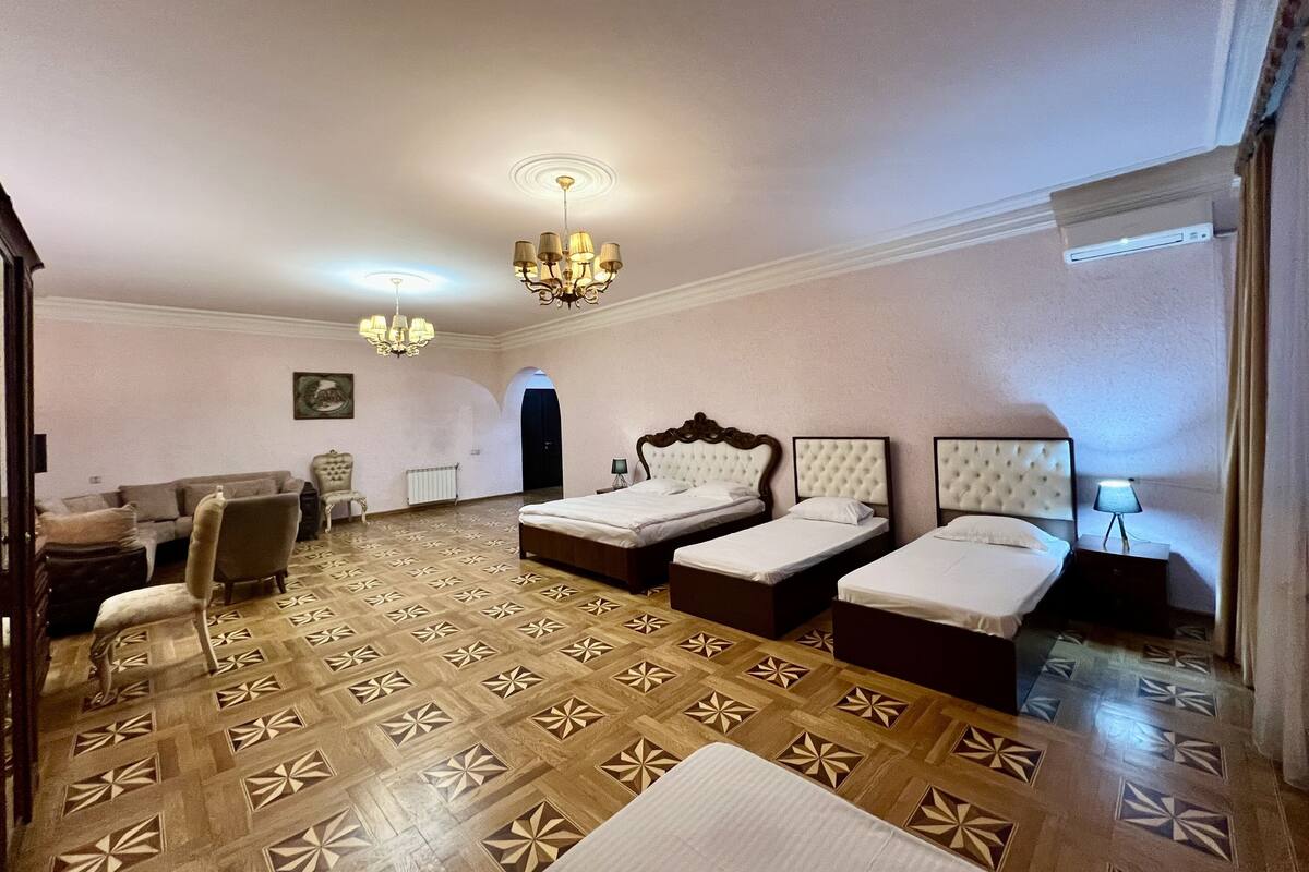 A hotel room with three beds, a sofa, a chair, and a chandelier.