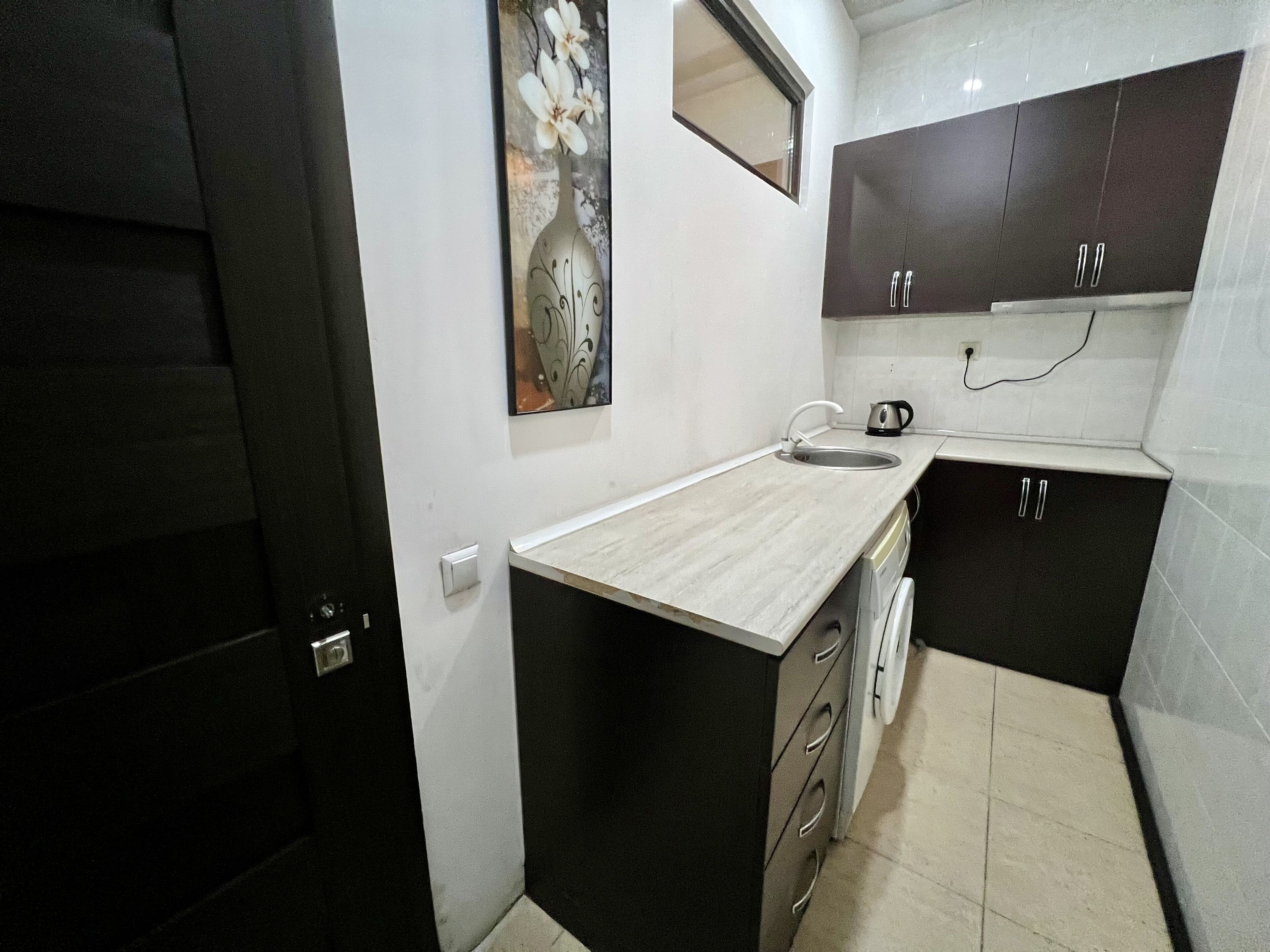 A compact kitchen with a sink, a kettle, and dark cabinets.
