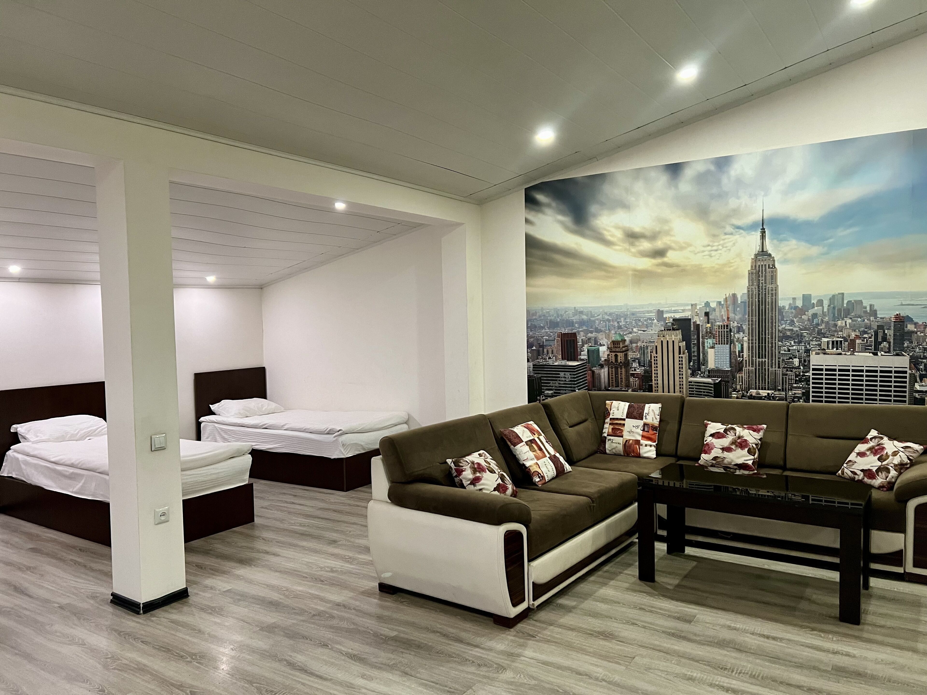 Une chambre d’hôtel avec une fresque murale représentant un paysage urbain, un canapé, deux lits et un plancher en bois.