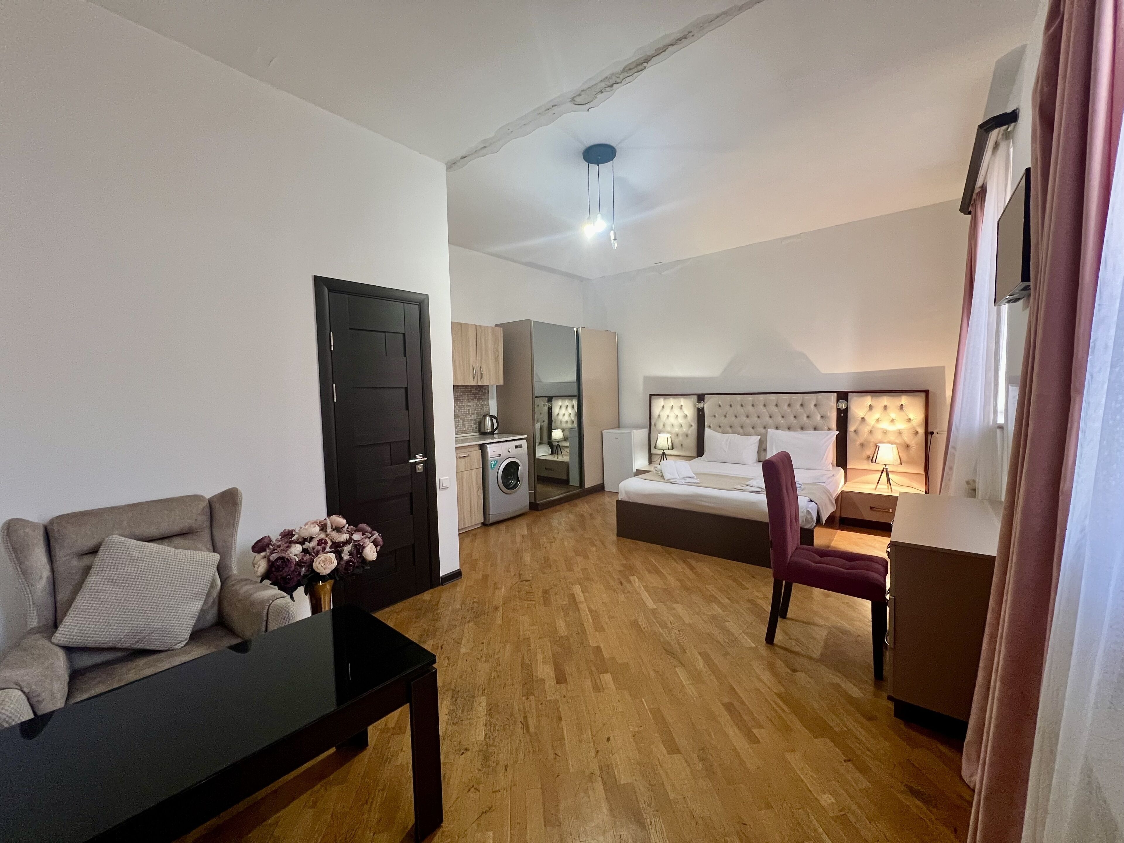 Una habitación moderna y bien iluminada con sofá, mesa de comedor, cama con cabecera, pequeña cocina y baño.