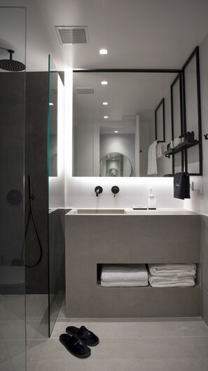 A modern bathroom with a glass shower enclosure, a white sink with a mirror above it, and a towel rack with towels.
