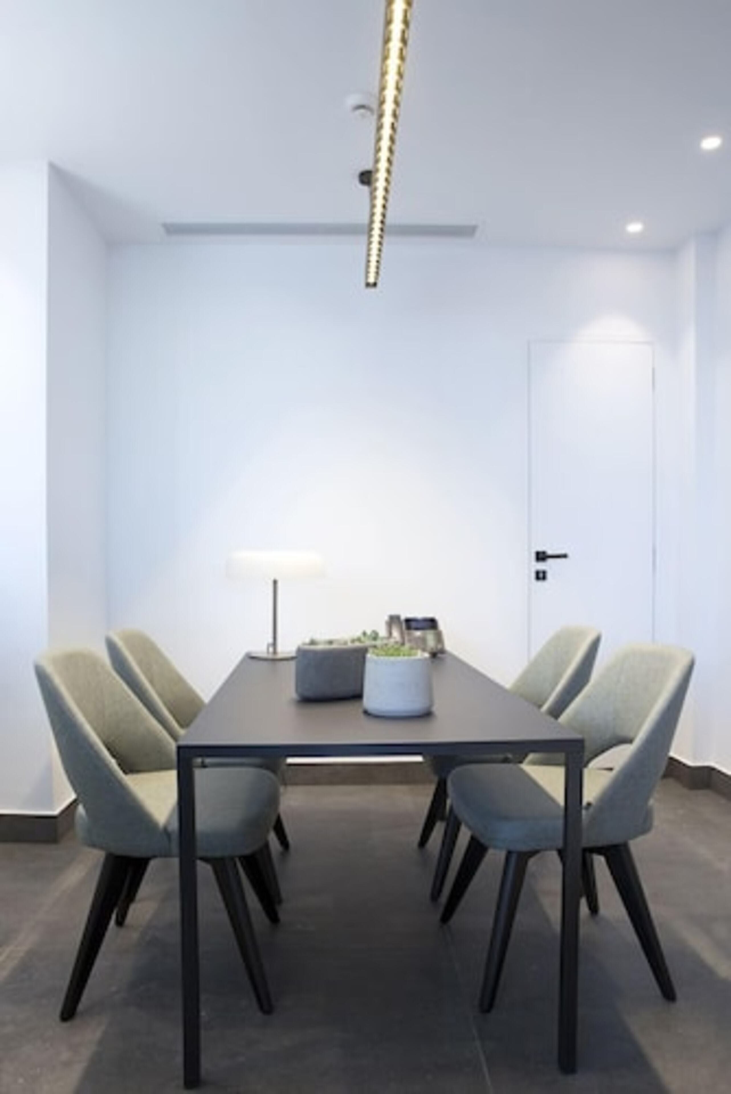 Un salón de conferencias con una mesa rectangular, cuatro sillas, una lámpara de pie y una puerta.