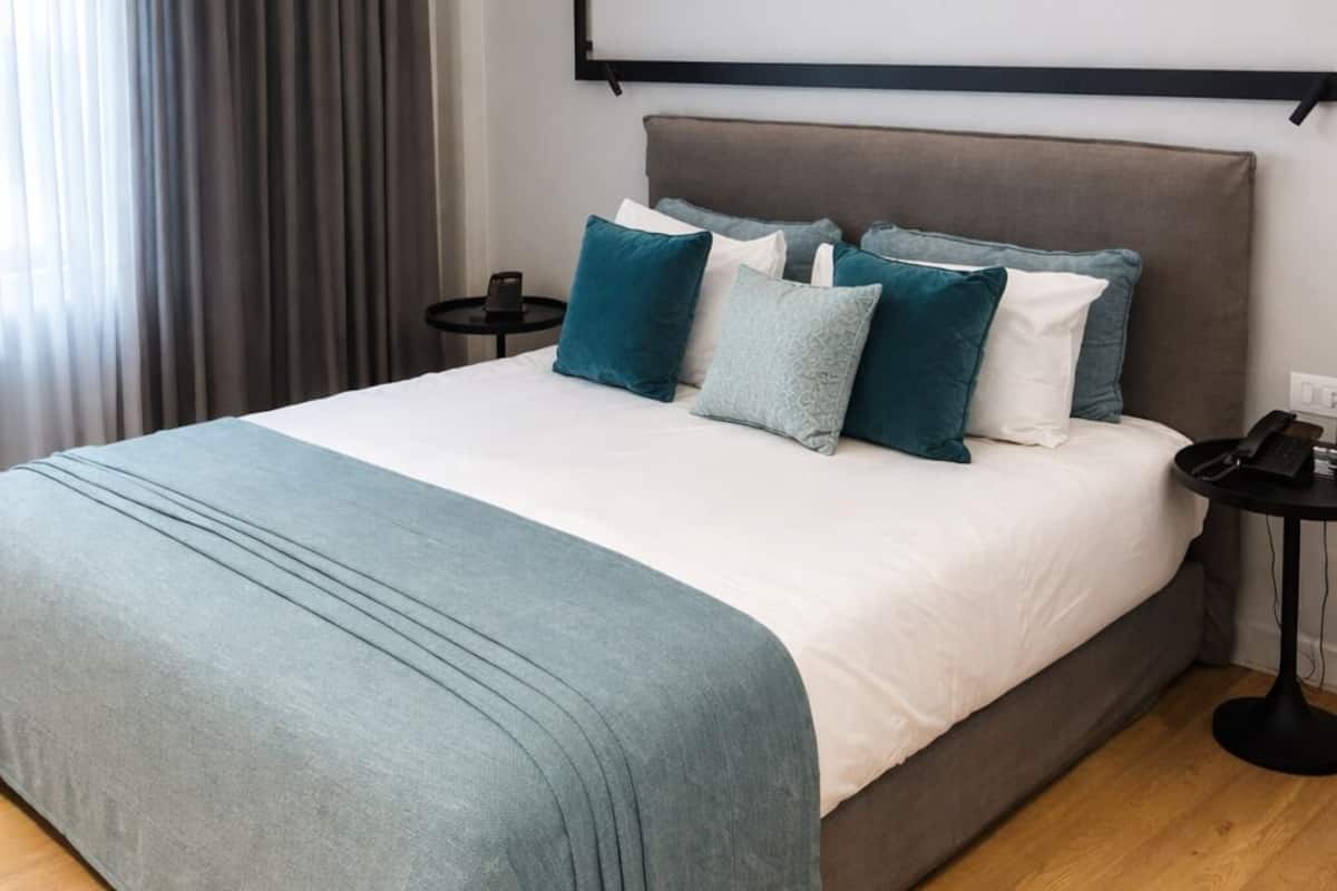 Una habitación de hotel moderna con una cama grande, una mesita de noche y un televisor montado en la pared.
