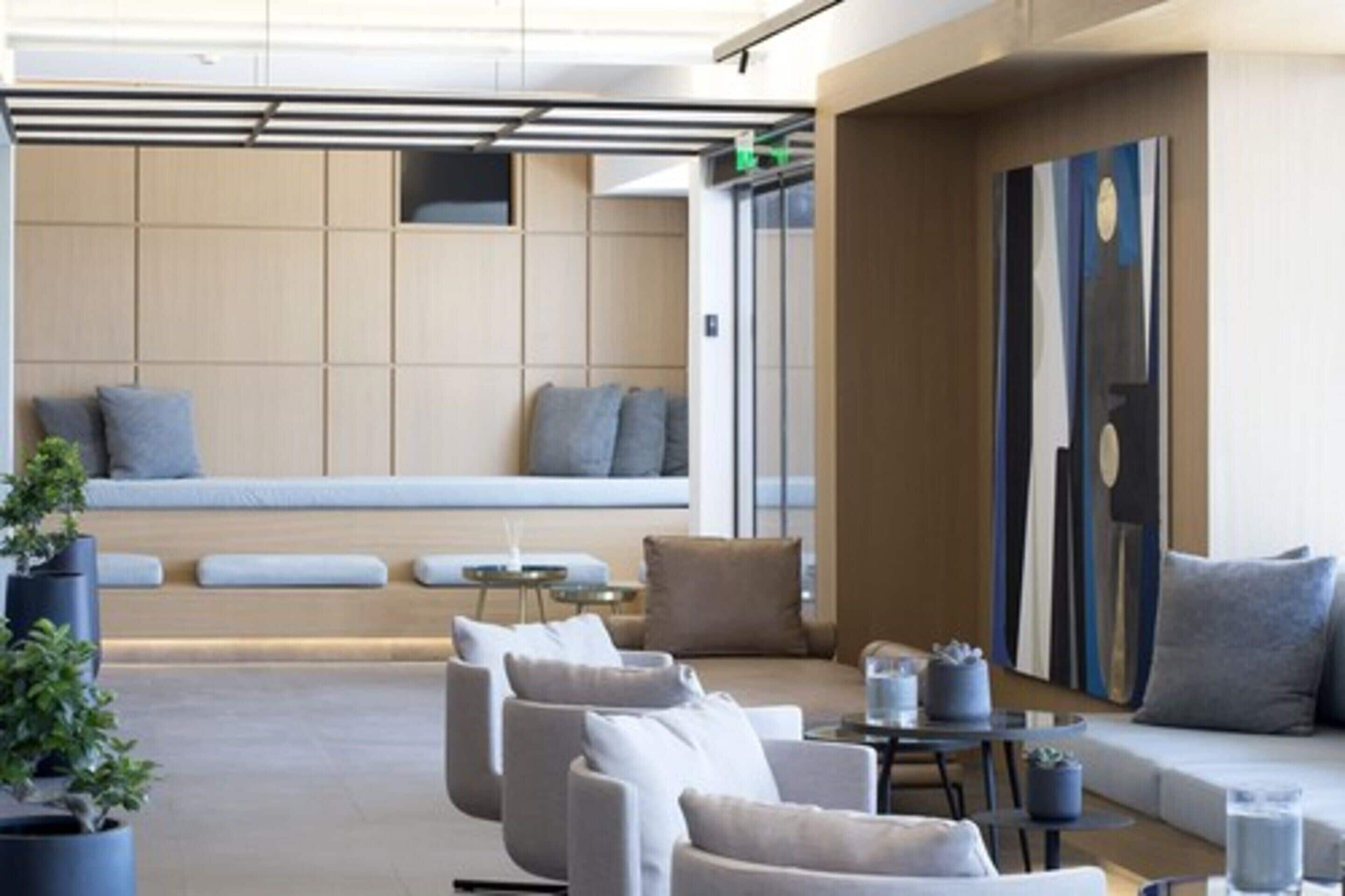 Een moderne lounge met zitplaatsen en een bijzettafeltje, een groot abstract schilderij aan de muur, en een wand van houten panelen op de achtergrond.