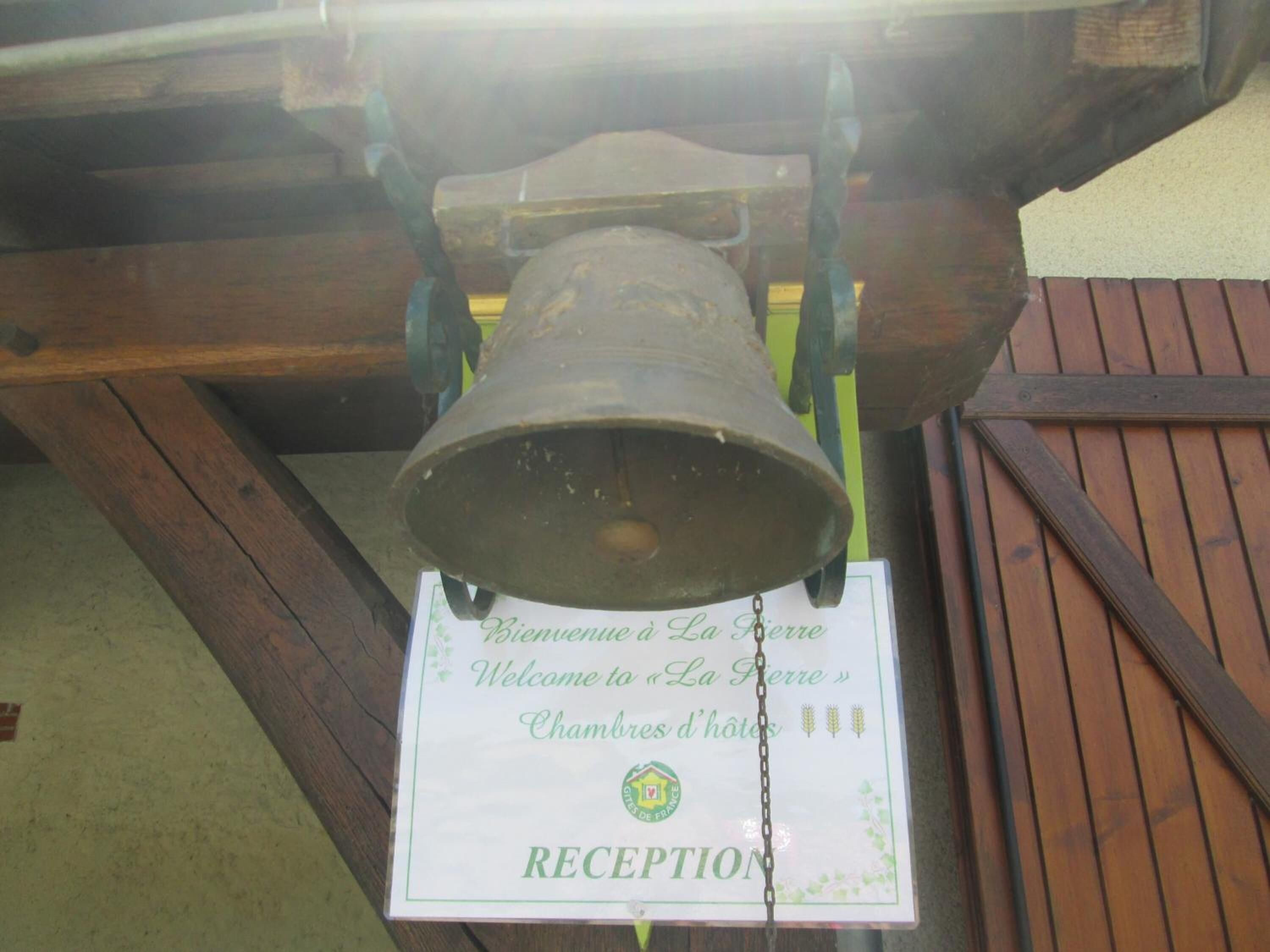 A bell hanging from a wooden structure with a sign below it that reads "RECEPTION" and "Bienvenue à La Pierre Chambres d'hôtes".