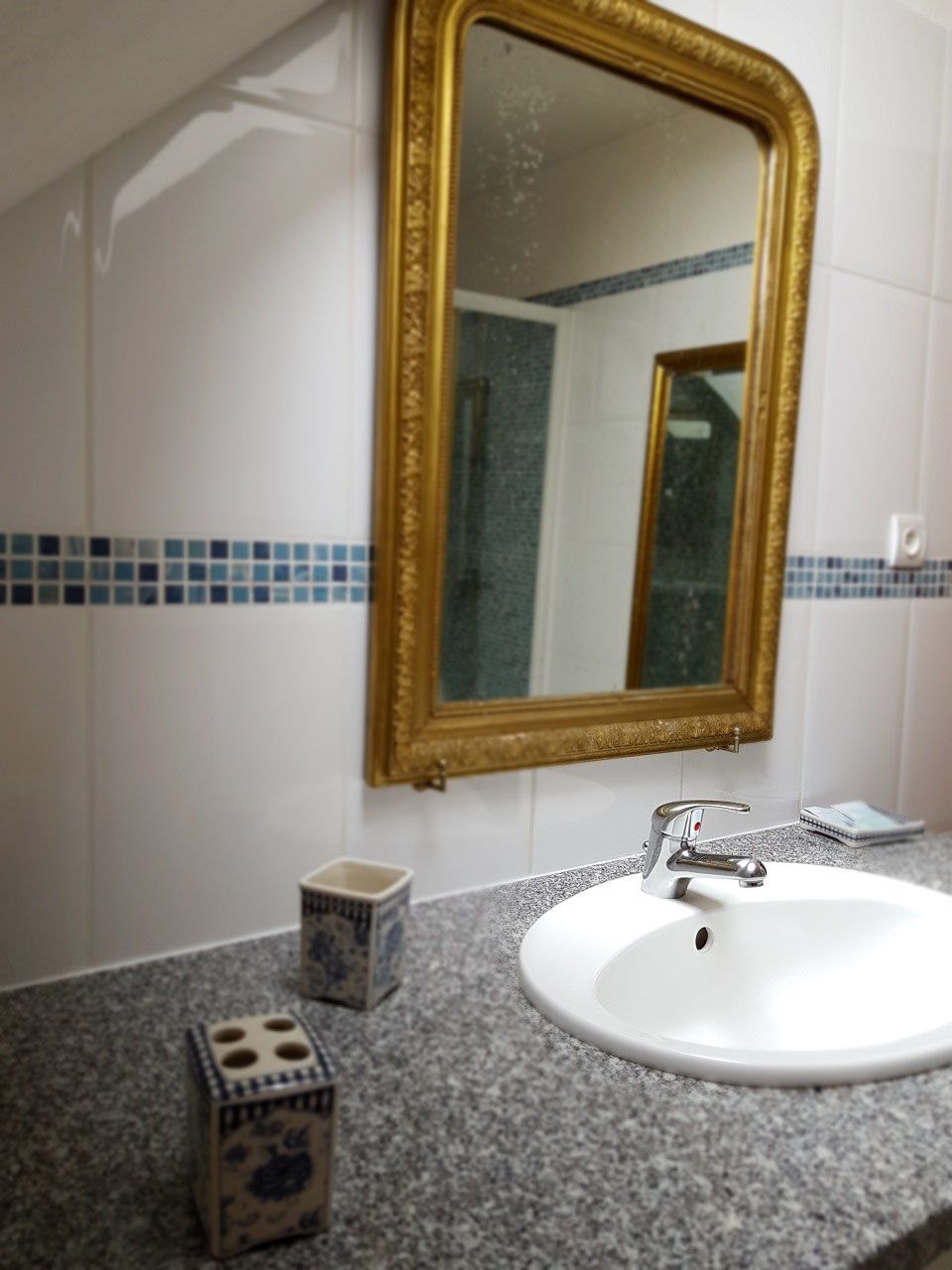 A bathroom with a white sink, a gold-framed mirror, and blue-tiled walls.
