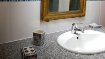 Un baño con un lavamanos blanco, un espejo con marco dorado y paredes de azulejos azules.