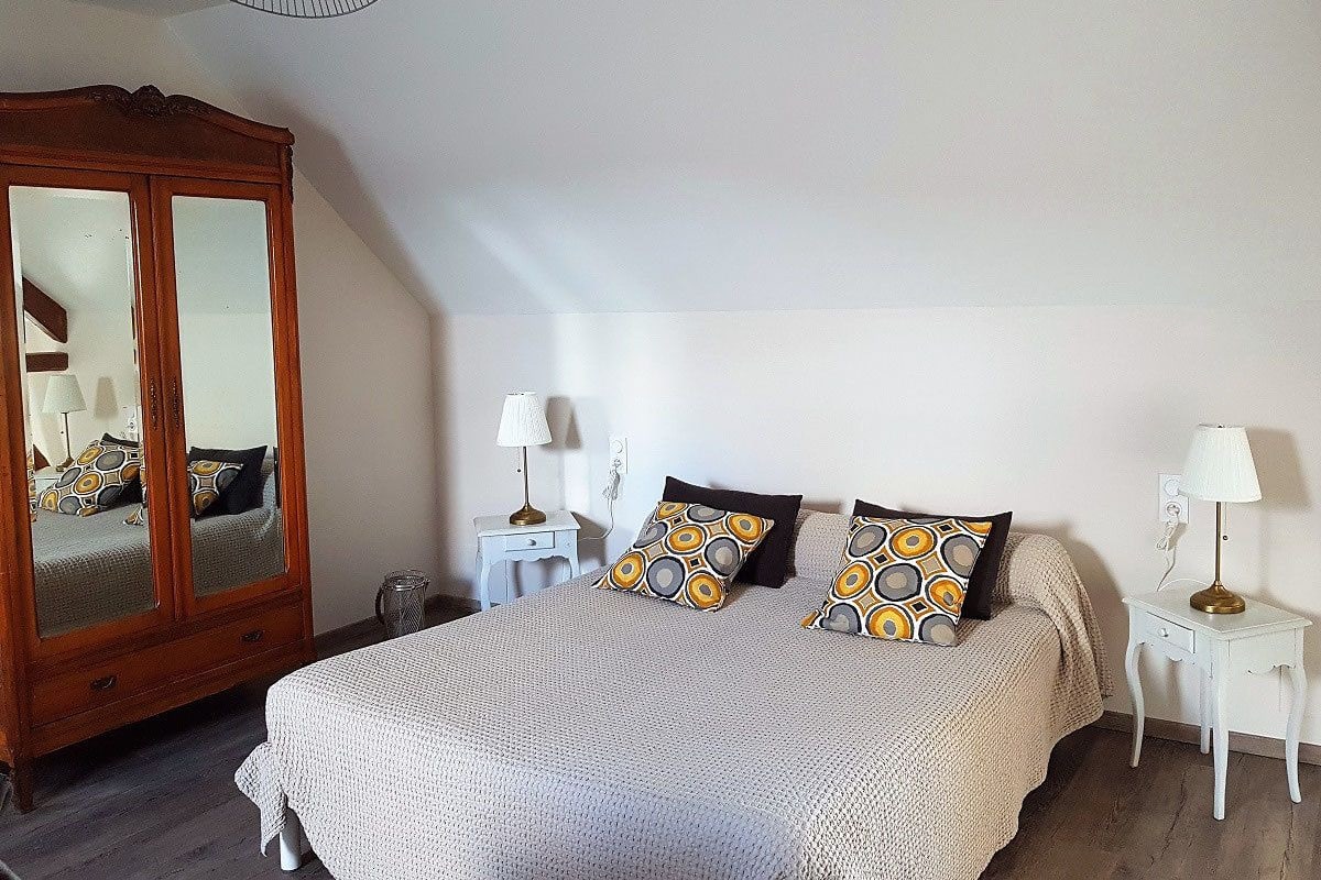A bedroom with a large bed, a wooden wardrobe, two bedside tables with lamps, and a hanging light fixture.