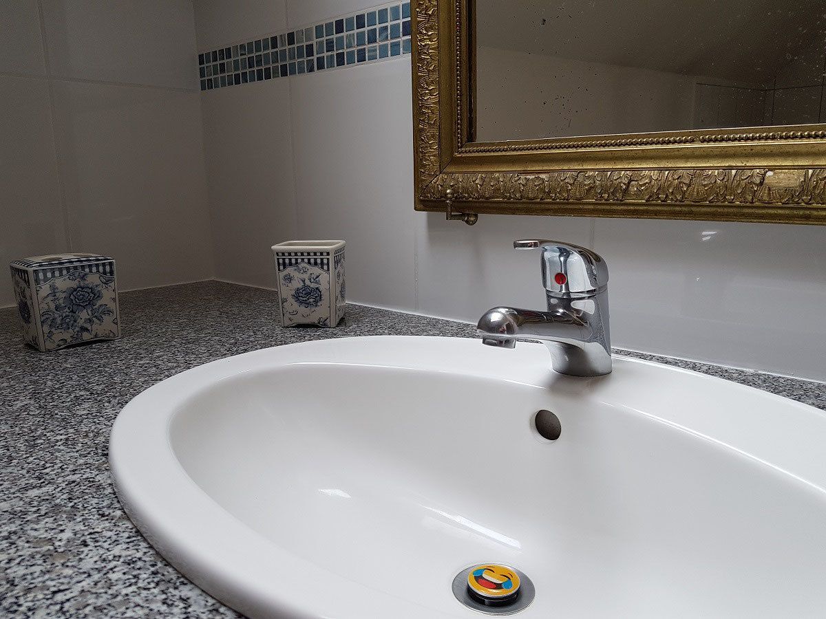Un baño con un lavamanos blanco, un espejo con marco dorado y dos jarrones decorativos en el suelo.