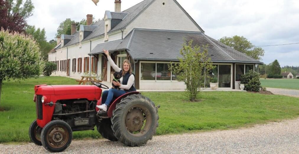 A person on a red tractor in front of a large house with a covered porch.