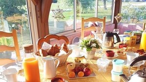 A breakfast table set with bread, pastries, fruits, and beverages, with a view of greenery outside. - Le Champ du Pre (Gievres)