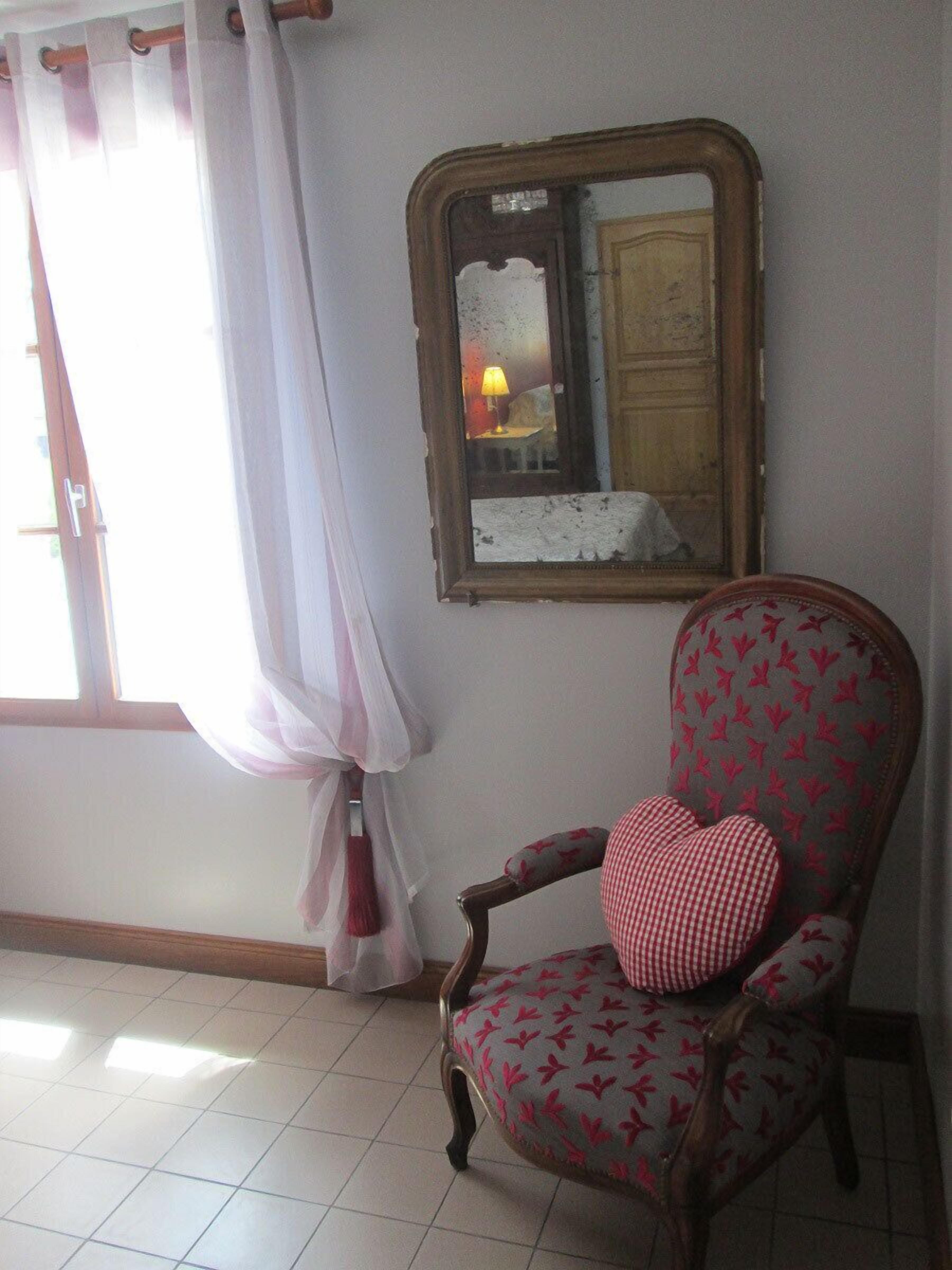 A room with a chair, a window with curtains, and a mirror on the wall.