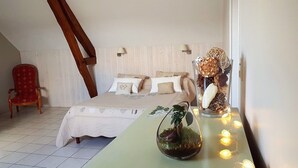 A cozy bedroom with a bed, a red chair, a wooden beam, and a decorative plant on a table. - Le Champ du Pre (Gievres)