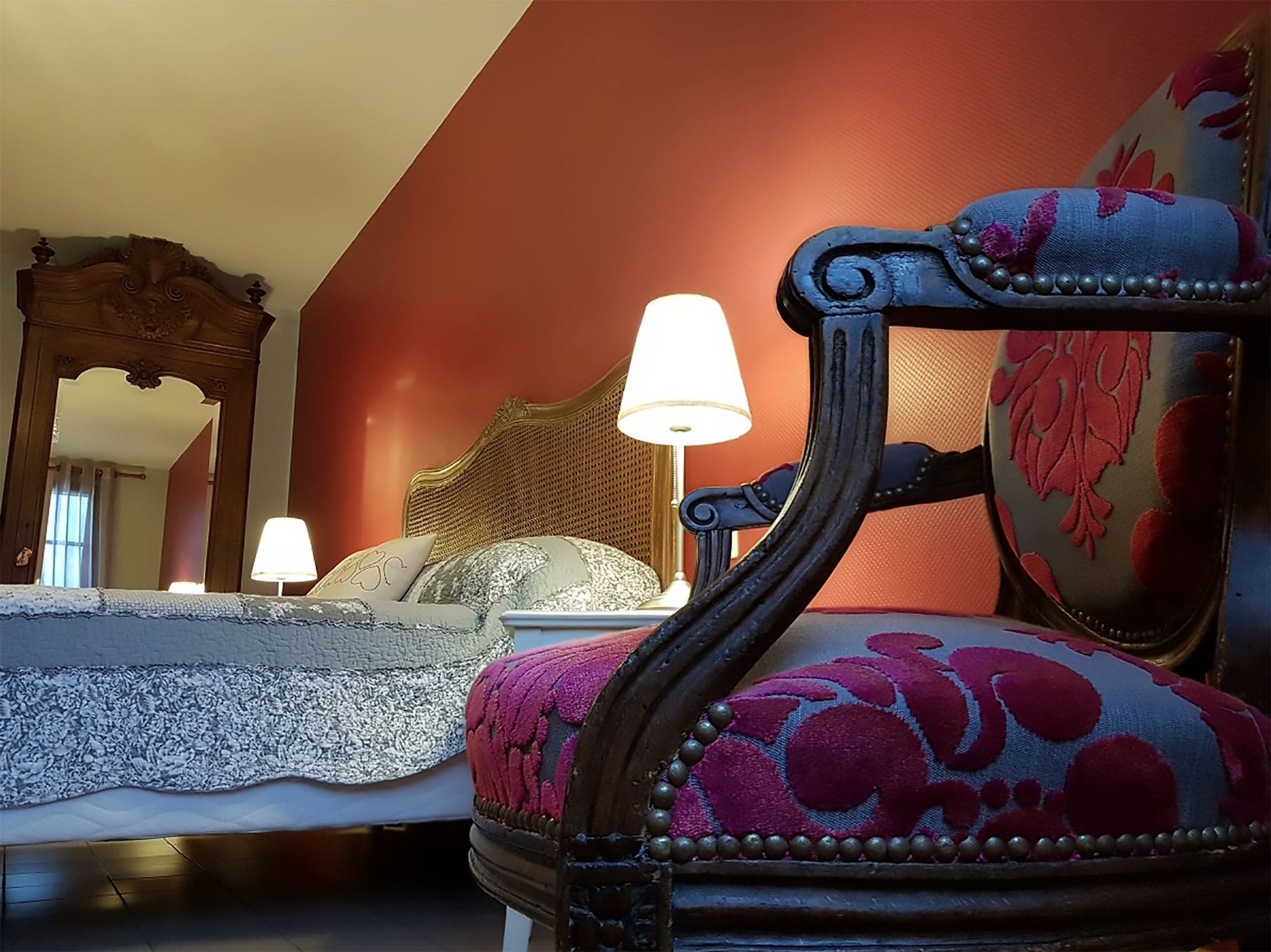 A bedroom with a bed, a nightstand, a lamp, a chair, and a mirror.