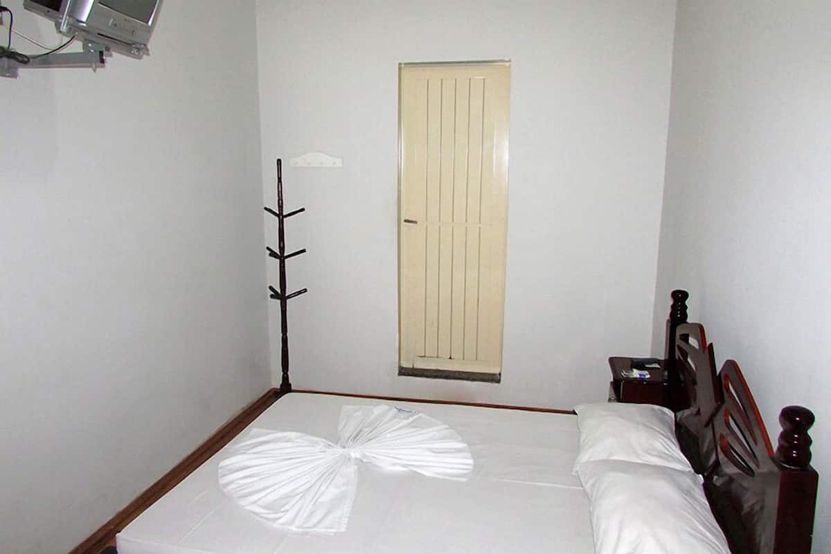 Un dormitorio con cama, mesita de noche, lámpara y ventana con puerta cerrada.