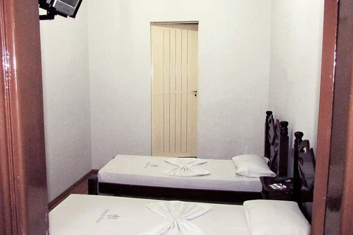 Habitación de hotel estrecha con dos camas individuales, un cabecero de madera y una puerta al fondo.