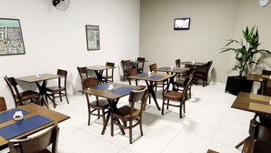 A hotel dining area with multiple tables and chairs, a clock on the wall, and a potted plant. - Grande Hotel Araçatuba (Aracatuba)