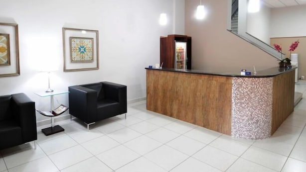 A reception area with a wooden reception desk, black seating, and framed artwork on the walls. - Grande Hotel Araçatuba (Aracatuba)