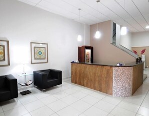 A reception area with a wooden reception desk, black seating, and framed artwork on the walls. - Grande Hotel Araçatuba (Aracatuba)
