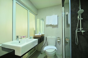A modern bathroom with a white sink, mirror, and toilet. There is a shower area with a glass door and a towel hanging on the wall.