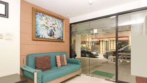 A reception area with a teal sofa, a framed floral painting, and a glass door leading outside. - OYO 225 Premier Place Hotel (Bangkok)