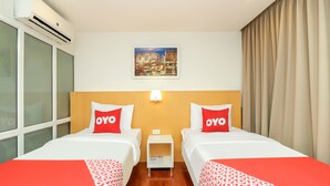 A hotel room with two beds, each with a red and white patterned bedspread, a small bedside table, a wall-mounted lamp, and a painting above the beds. - OYO 225 Premier Place Hotel (Bangkok)