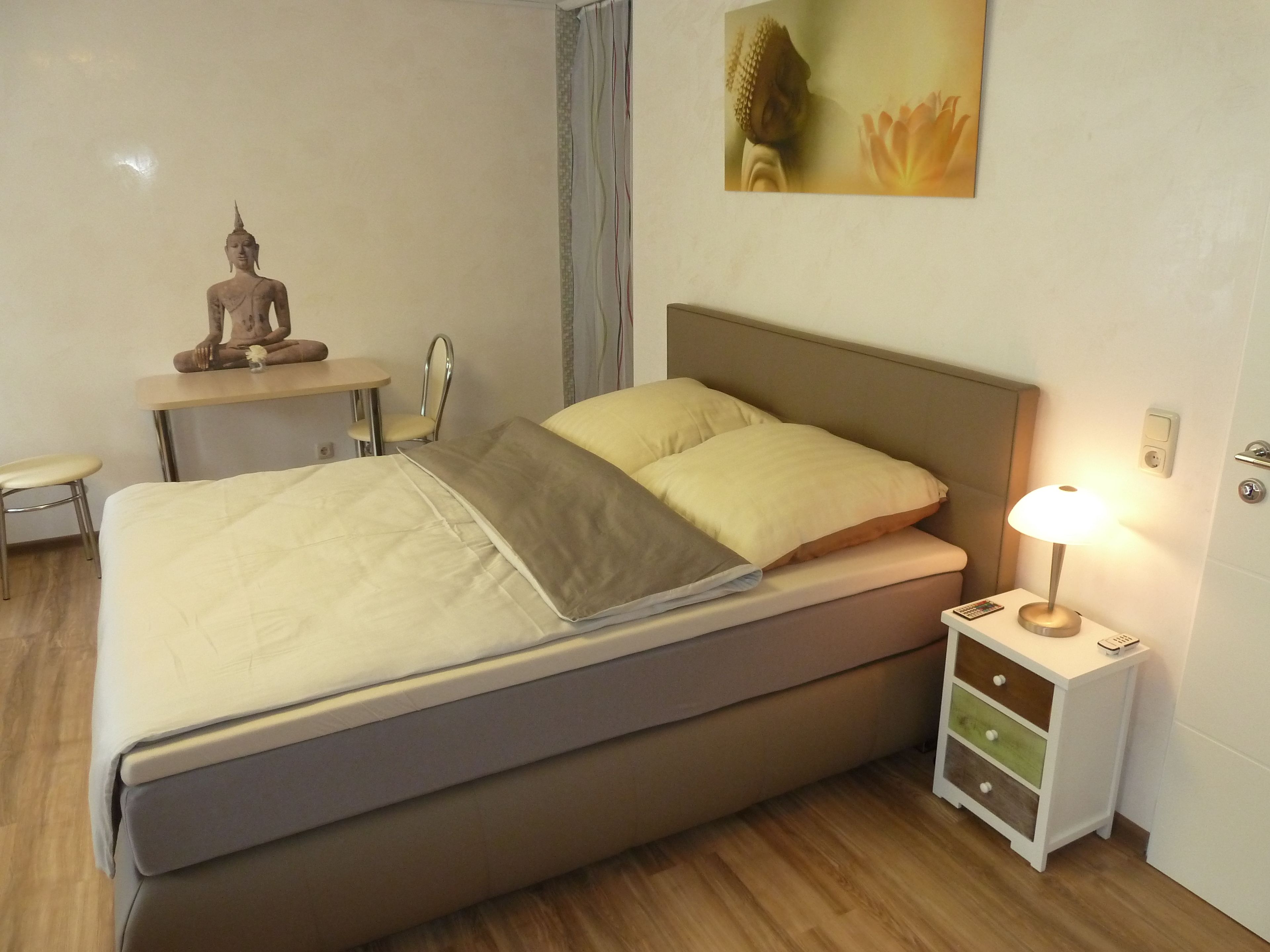 Een keurig opgemaakte slaapkamer met een bed, nachtkastje, lamp en een beeldje.