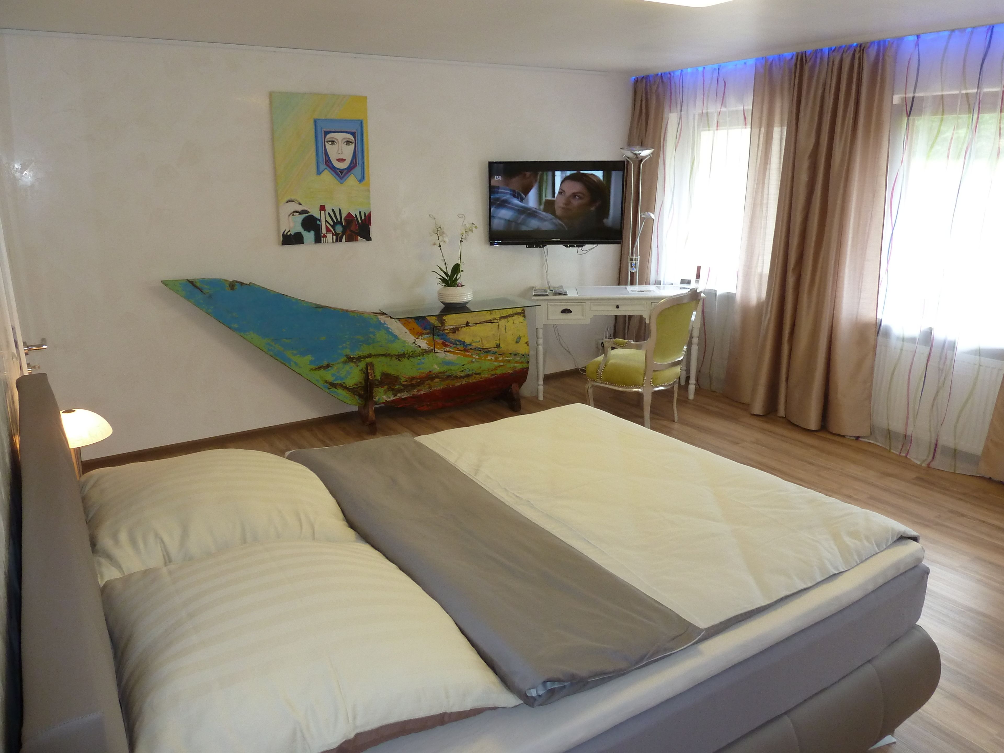 Une chambre d’hôtel avec un lit, un bureau et une chaise, une télévision et une œuvre d’art colorée accrochée au mur.