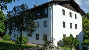A two-story building with a white facade and dark roof, surrounded by greenery and trees. - Ferienwohnung Jeremy (Bad Toelz)