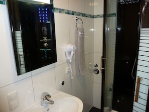 A bathroom with a white sink, a towel rack, a glass shower enclosure, and a wall-mounted control panel.