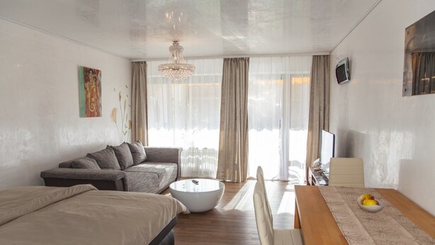 A modern, well-lit room with a sofa, a round coffee table, a dining table with chairs, and a television. - Ferienwohnung Royal (Bad Toelz)