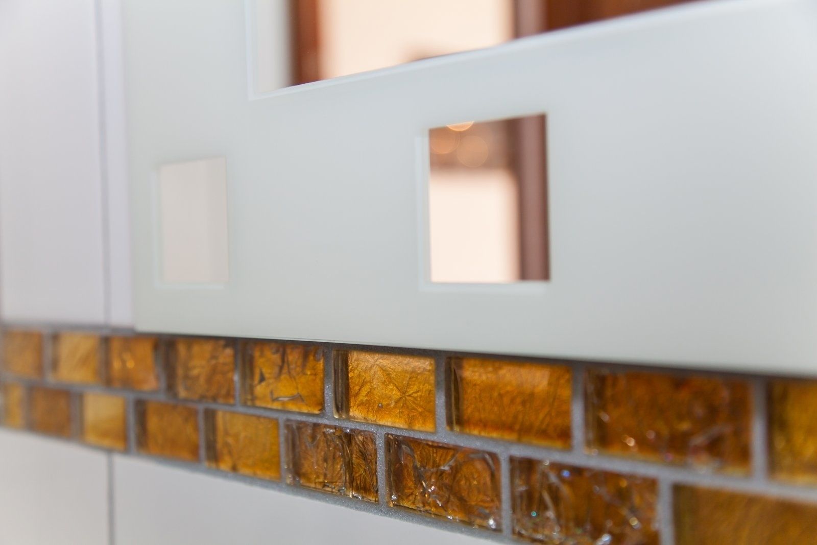 Ein Detailaufnahme eines weißen Schranks mit einer Glasrückwand, die ein gold- und braunes Mosaikmuster zeigt.