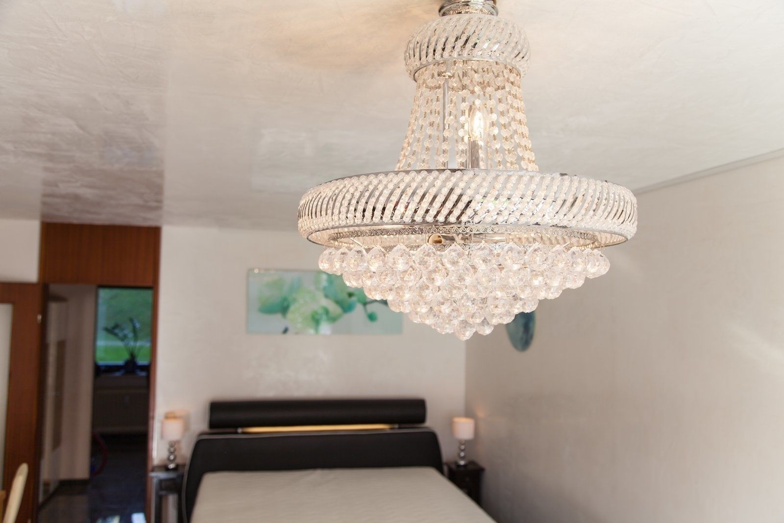 Ein Kronleuchter in einem Schlafzimmer mit Bett, Nachttisch und einem Gemälde an der Wand.