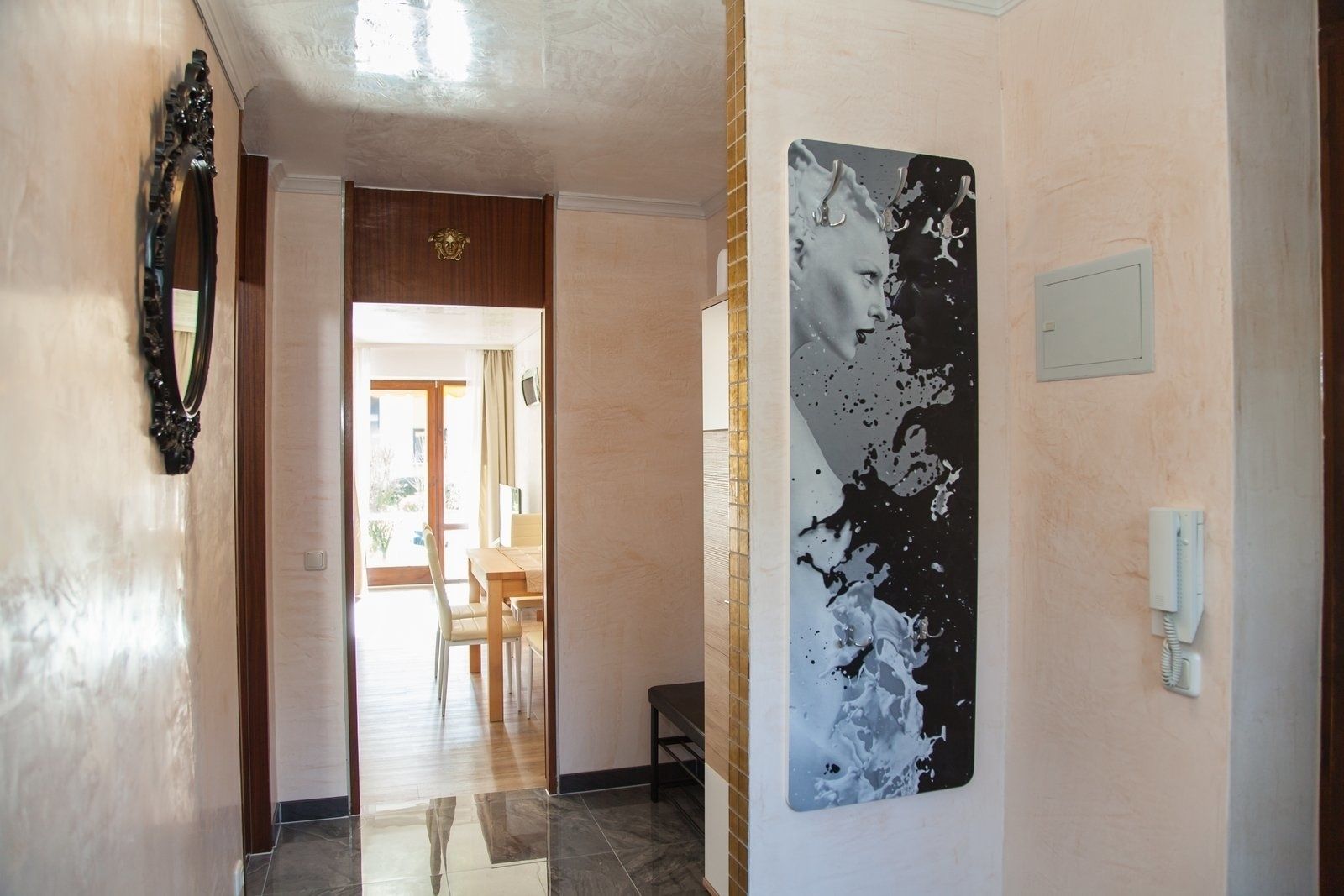 A hallway with a wooden door, a large abstract painting, and a telephone on the wall.