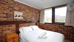 Habitación de hotel con pared de ladrillo, cama con ropa blanca, mesita de noche de madera y ventana con cortinas.