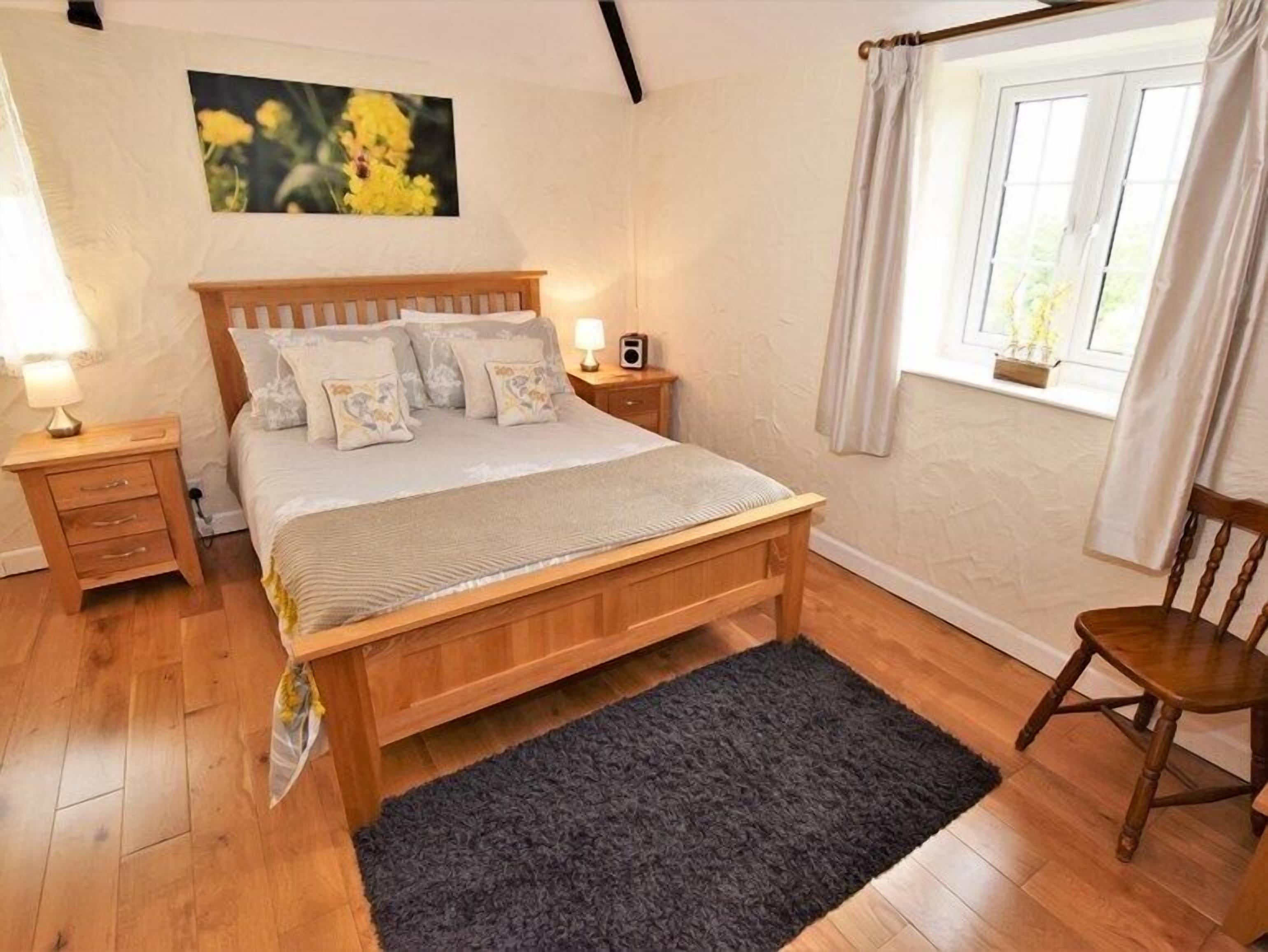 Une chambre à coucher avec un lit en bois, deux tables de chevet, une commode, une fenêtre avec des rideaux et un tableau accroché au mur.