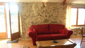 A room with a stone wall, wooden floor, red sofa, and a wooden coffee table. - Beautiful renovated stone barn with magnificent view! Quiet village (Rabouillet)
