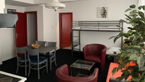A compact room with a bunk bed, a dining table with chairs, a small table with a glass top, a red armchair, and a potted plant. - Apartment Backhouse (Ostend)